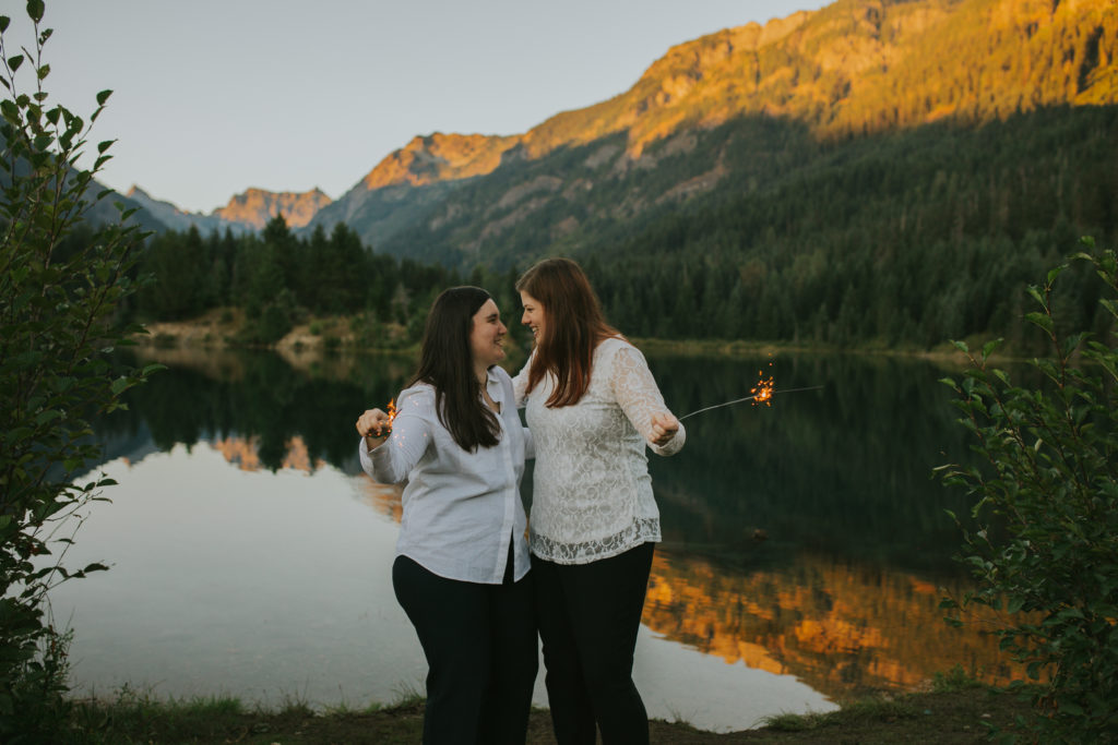 queer couple holding sparkles near a lake