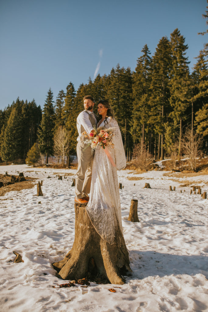 Washington elopement couple in the snow standing on a tree stump 