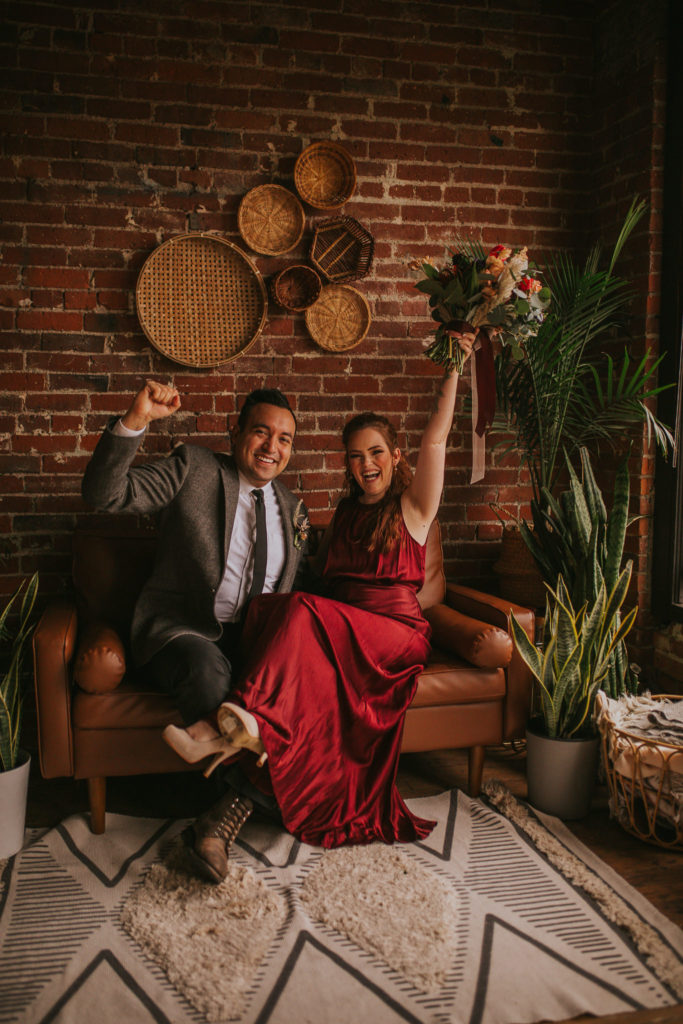 girl in red dress and man in suit sitting on a couch celebrating