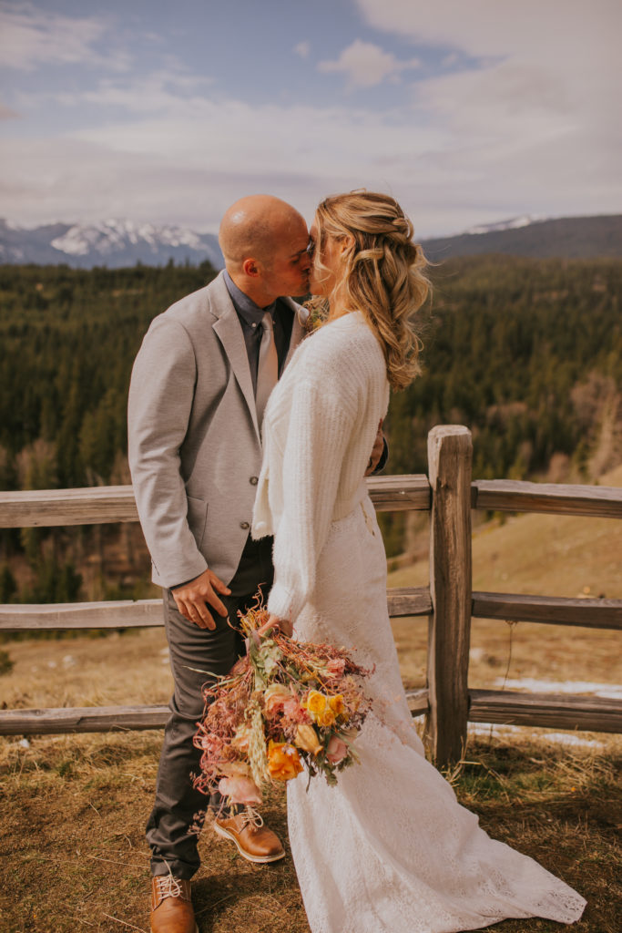 wedding bride and groom standing by a fence kissing each other with a forest landscape