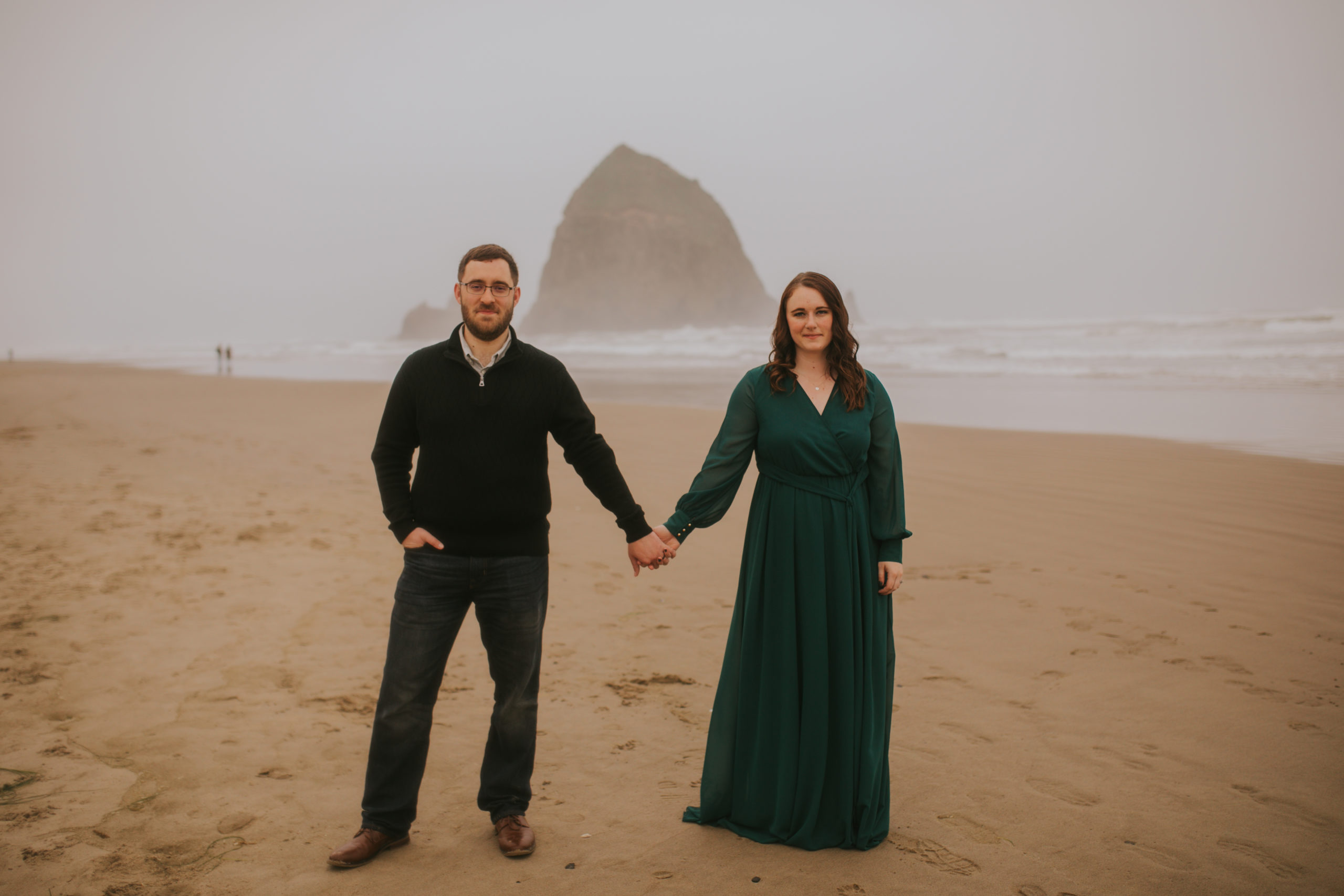Couple standing facing the camera with Haystack Rock Cannon Beach in the background