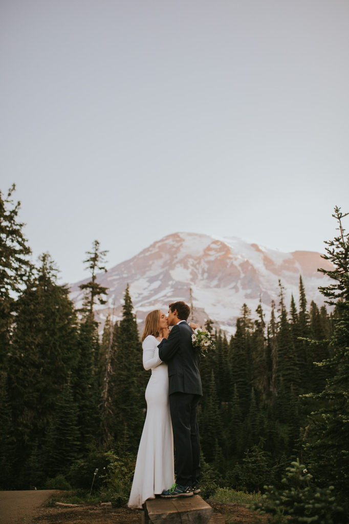 Wedding couple standing on top of a bench kissing with Mount Rainier behind them in the background