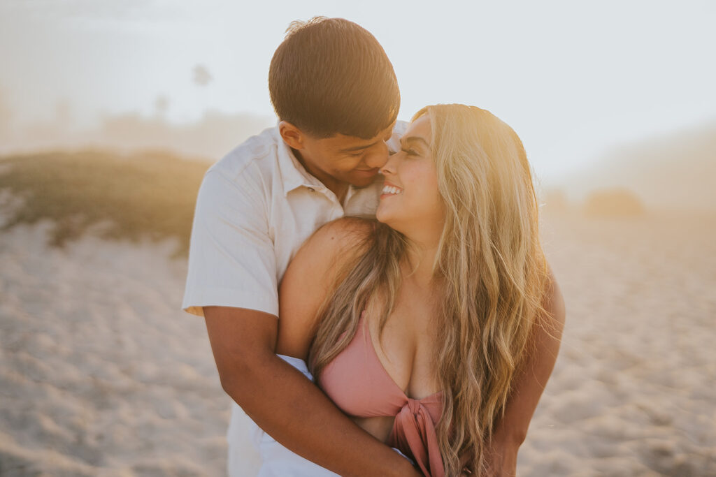 couple standing together on the beach. Man is hugging woman from behind and they are looking at each other